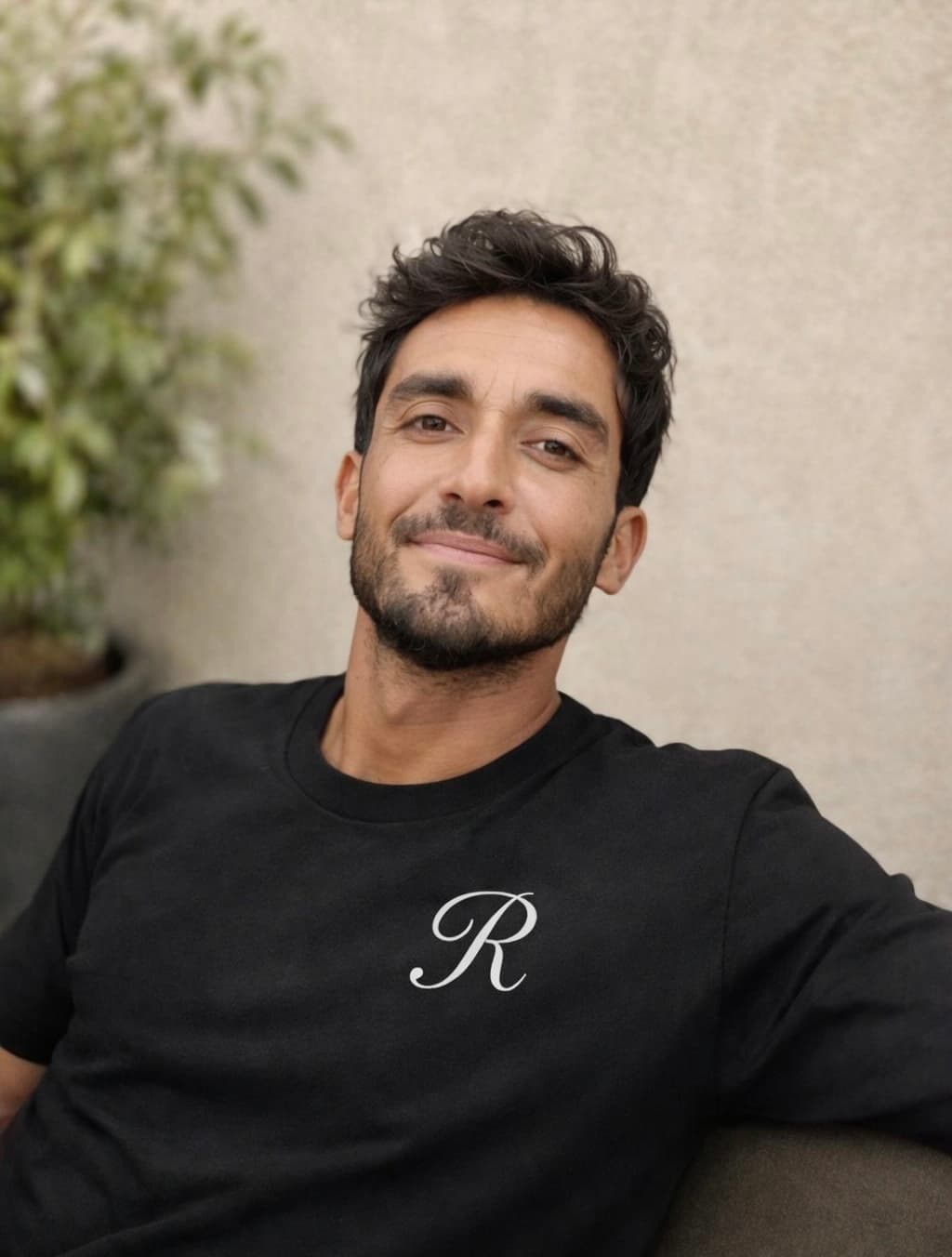 Smiling man with dark hair and beard wearing a black shirt with a cursive R.